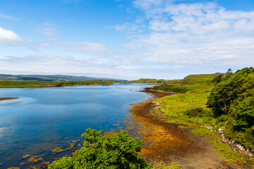 Loch Dunvegan - peaceful coastal lake landscape with green hills, blue sky, and calm water near the shoreline in Scotland