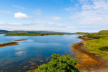 Loch Dunvegan - peaceful coastal lake landscape with green hills, blue sky, and calm water near the shoreline in Scotland