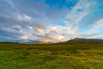 Fototapeta premium On the NC500, Scotland, open grassland landscape with distant hills under blue sky and dramatic clouds