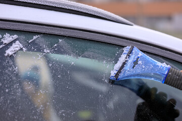 Scraping a frozen window with a plastic scraper on a frosty morning