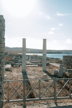 Scenic view of Delos island featuring ancient Greek ruins, standing columns, scattered marble blocks illuminated by warm summer light.