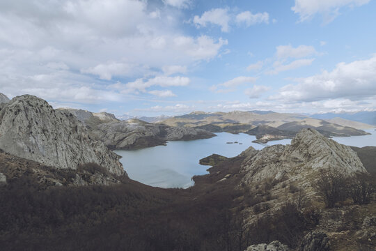View of jagged, rocky mountains embracing the tranquil lake under a vast, blue sky dotted with fluffy clouds, Pico Gilbo, Castilla y Le&oacute;n, Spain.