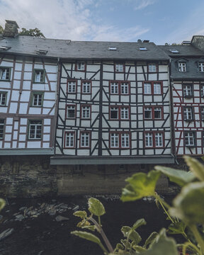 View of timbered houses stand tall with white walls and red window frames beneath a blue sky, where the past whispers stories, Monschau, North Rhine-Westphalia, Germany.