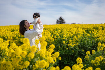 なの花畑で赤ちゃんを抱っこする母親