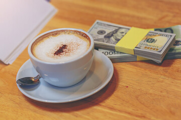 A cup of cappuccino with bundle of US dollars on the table, Business negotiations. wealth and investment concept.