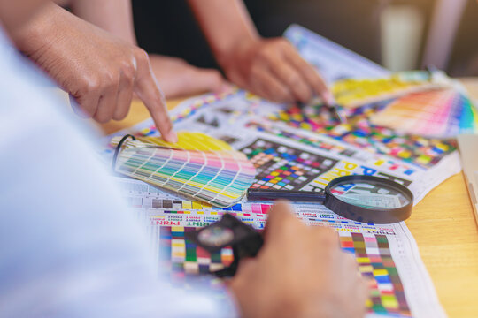 Team graphic designer checking print quality of media graphics proof print and color guides in printing industry. Selected focus