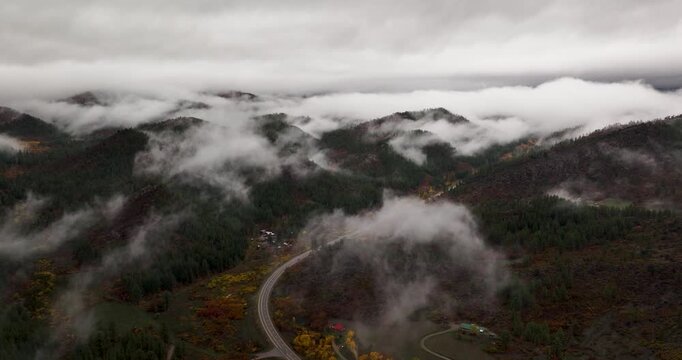 A high-flying aerial drone shot over the scenic Route 160 in Colorado, with low-lying clouds and fog sporadically covering the vibrant autumn foliage showcasing the beauty of fall in the Rockies.