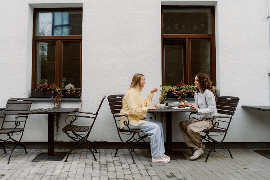 Two friends share a delightful brunch at a charming outdoor cafe. Surrounded by flowers, they smile and savor delicious food and drinks under the warm sun.