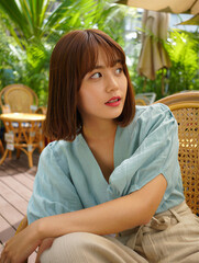 Young woman in casual attire sits outdoors bathed in soft sunlight surrounded by lush greenery.