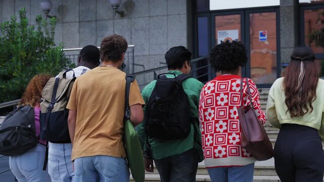 Group of unrecognizable students seen with their backs turned, climbing a flight of stairs to enter the university building. Young academic people on the university campus on their way to class