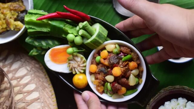 Top-view still life of authentic Nam Prik Long Ruea, a traditional Thai chili paste dip, presented in ceramic bowls on a wooden board and banana leaf. The composition includes fresh seasonal vegetable