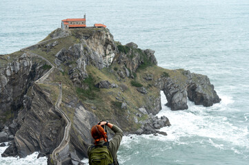 Woman photographer taking pictures of San Juan de Gaztelugatxe hermitage.