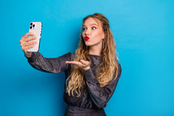 Stylish girl takes a playful selfie against a bright blue background wearing a shiny dress and glamorous makeup for fashion holiday and party themed stock photo