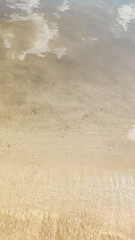 Transparent water ripples over a sandy beach with sky reflections