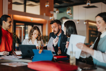 A diverse group of people sits around a table, discussing documents and sipping drinks in a lively cafe. They share ideas, review charts, and collaborate like a team of coworkers.