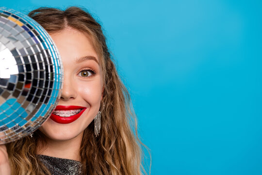 Glamorous young woman with a disco ball in a bright blue studio showcasing party fashion makeup glamour and festive vibe