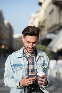 Young man drinking coffee to go and looking smartphone in the city