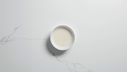 Minimalist flat lay of creamy white liquid in a bowl on Carrara marble background.