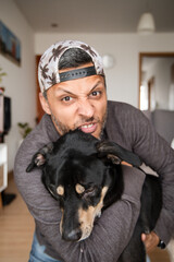 A man is hugging a black dog with a hat on his head