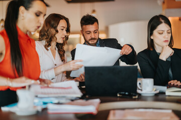 Colleagues collaborate over documents and charts in an office, discussing strategies and reviewing paperwork. Coworkers share ideas and stay focused on the task, creating a productive atmosphere.