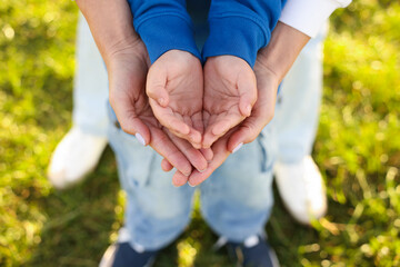 Mother holding hands with her son outdoors, closeup. Family bonding