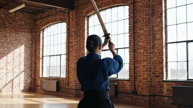 Woman practicing kendo with a sword in a large room