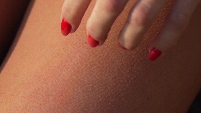 Goosebumps skin touch. Woman's hand with red nail polish gently touches her thigh, creating goosebumps on her fair skin.
