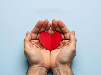 Man's hands holding a red paper heart on a blue background. Love, charity, and health care concept for Father's Day or Valentine's Day. Donation and kindness symbol with copy space