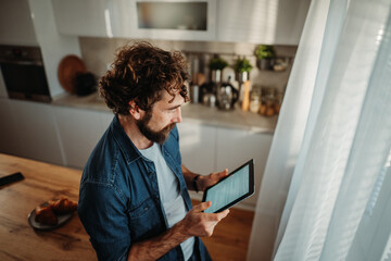 Man reading news on digital tablet in kitchen
