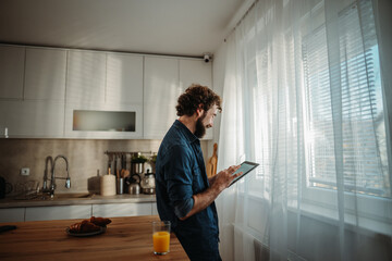 Man enjoying breakfast in kitchen using digital tablet