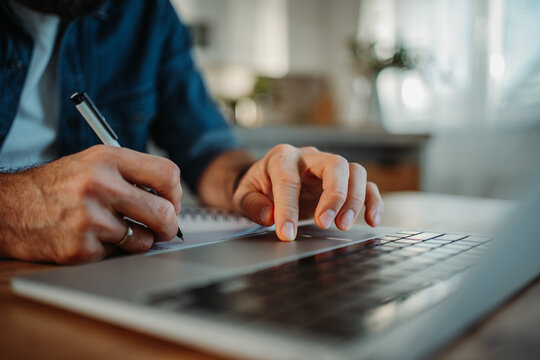 Man taking notes while working on laptop