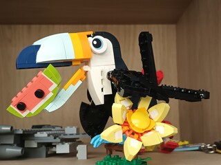 Naklejka premium Colorful toucan made of building blocks holding a slice of watermelon and standing near a flower