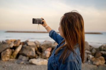 Woman taking a selfie by the sea at sunset on a rocky shore