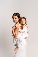 mother and child girl on a white cyclorama background, mother and daughter in a white suit hugging and kissing while playing, portrait, place and space for text