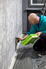 A focused man attentively applies decorative plaster to a wall with a spatula, demonstrating skill and precision during interior home renovation with care.