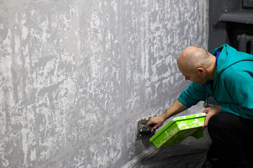 Man skillfully applies decorative plaster to a wall, enhancing the interior of an apartment with unique textures and designs using a trowel and plaster mix, showcasing craftsmanship and attention to