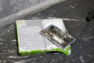 Close up, home renovation concept showing a paint tray filled with gray paint and a roller for painting walls, and plastic sheet, for DIY projects and design improvements.