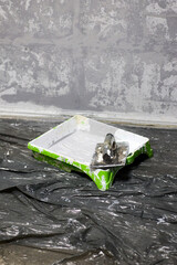 A close-up shows a paint tray filled with gray paint, with a tool resting on top, set on a plastic sheet indoors; this image captures the essence of a home renovation project, featuring a textured