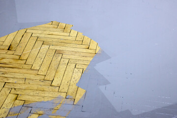 Intriguing perspective showcasing the restoration process of a wooden parquet floor, where new gray paint meets the classic herringbone pattern, emphasizing contrast and detail.