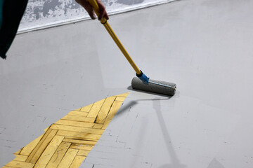 Refreshing a herringbone parquet floor with gray paint, using a paint roller for a home renovation project, creating a modern and stylish interior, DIY home improvement with painted floors.