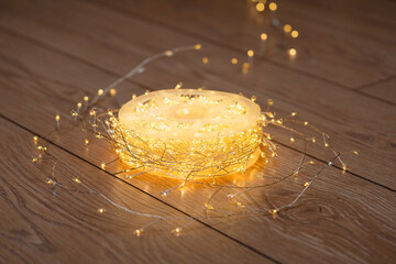 Christmas decorations. A spool of warm white LED lights softly glowing on a wooden floor. High resolution.