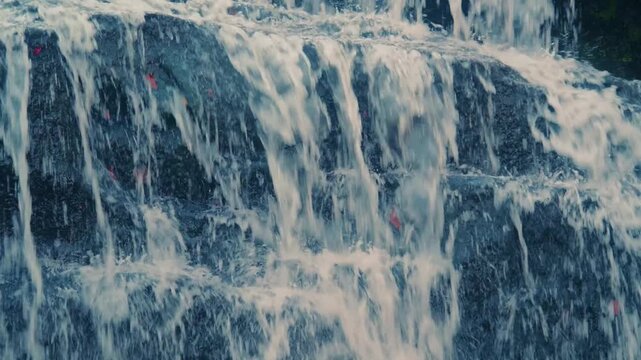 Close up footage of fresh, clear water flowing rapidly over dark, wet rocks at Glendale Falls in Massachusetts. The dynamic movement of the water creates white, frothy splashes, with small reddish spe