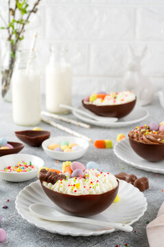 Easter dessert. Chocolate eggs with cheesecake filling decorated with chocolate candies and sugar sprinkles on a white plate on gray concrete background. Copy space.