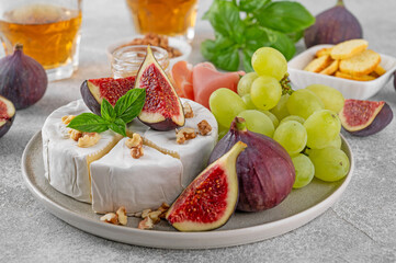 Camembert, bree cheese, walnuts, fresh figs, grapes, prosciutto and honey on a plate on a concrete background. Charcuterie plate. Top view