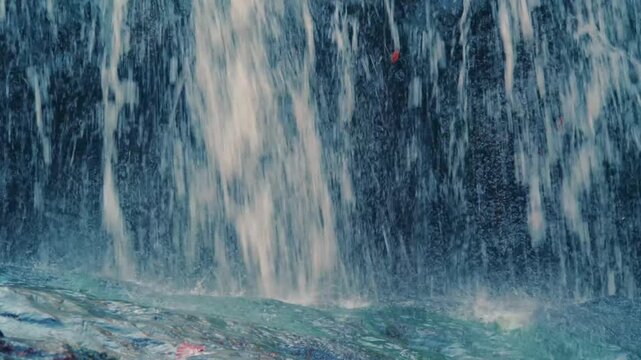 Close up shot of rushing water cascading over a rocky surface, with vibrant blue and white tones and small specks of red or orange.