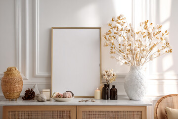A bright white room with elegant decorative elements including a blank canvas frame for art and a vase of dried flowers