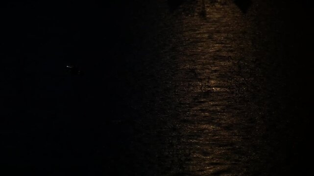 Raining at night on a swamp or pool of water with a reflection of yellow light on water, raindrops on water in dark night time.