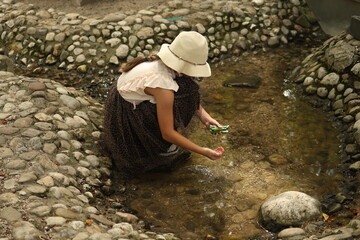 Girl in summer hat playing with water in a shallow stream.