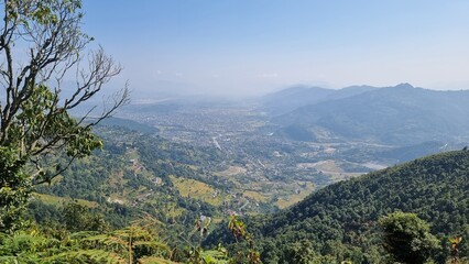 Panoramic view of a green Pokhara valley dotted with buildings, surrounded by verdant hills under a hazy sky