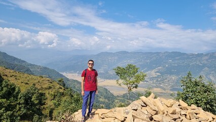 Naklejka premium Explorer standing on a mountain ridge, embracing a vast panoramic view of a scenic valley and distant hills under a bright sky, symbolizing freedom and adventure